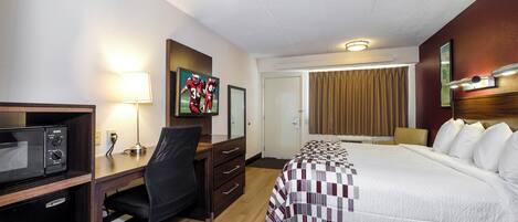 Habitación de hotel con cama, escritorio, silla, microondas y una obra de arte en la pared.