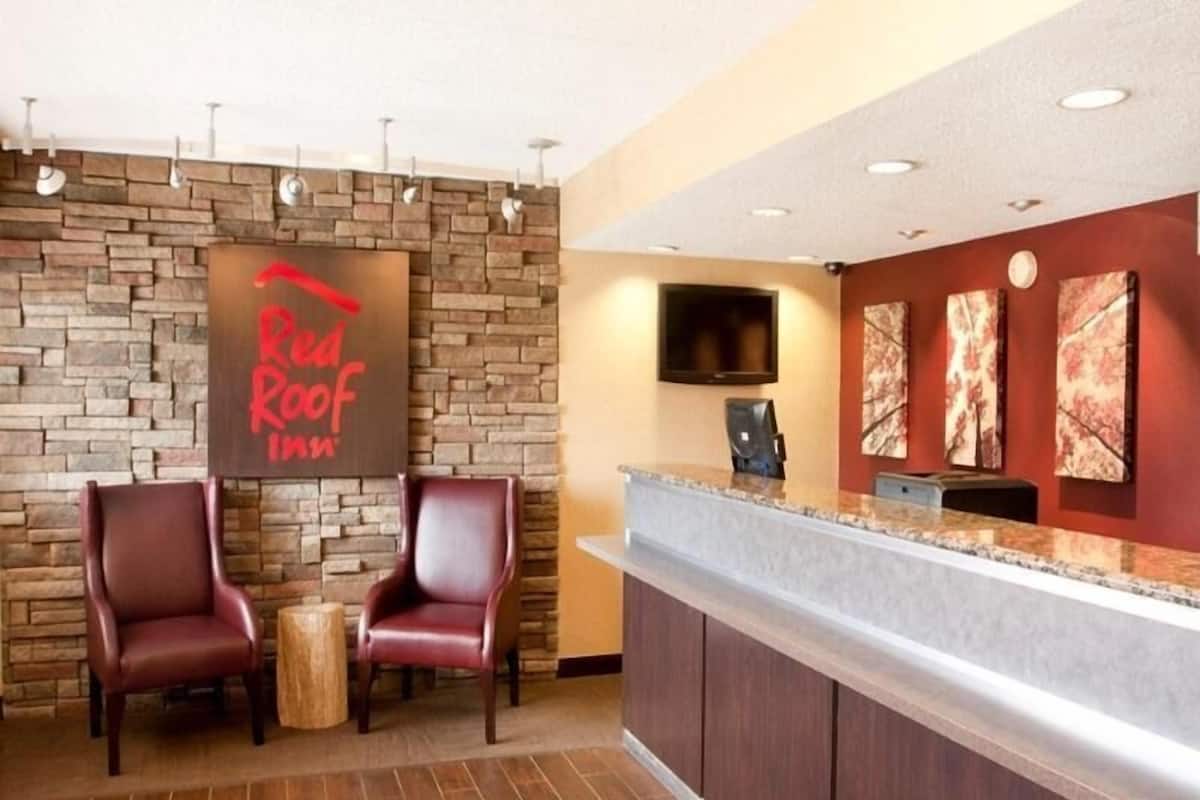 A reception area with a stone wall, two leather chairs, a wooden table, a reception desk, a flat-screen TV, and artwork on the wall.