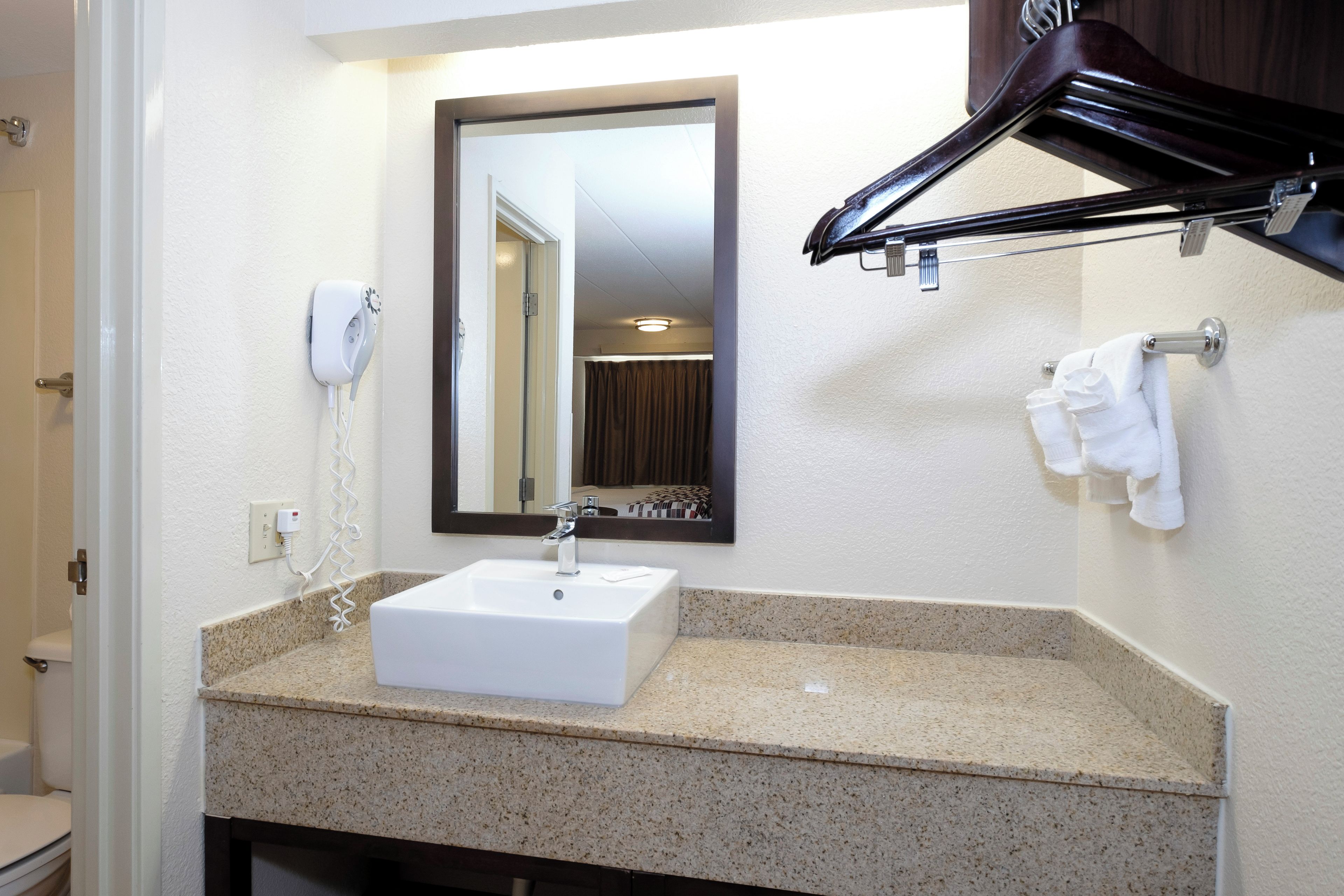 Un baño con un lavamanos blanco, un espejo, un perchero para toallas y un secador de pelo.