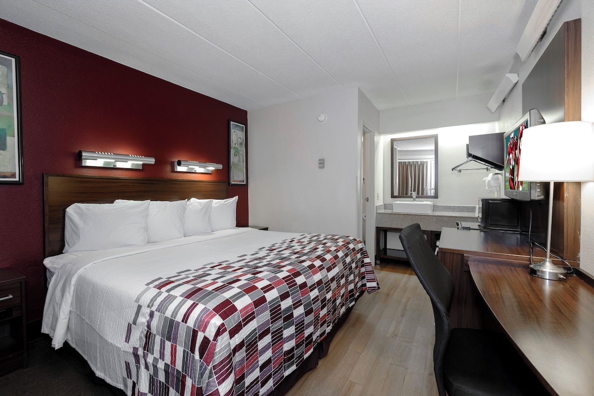 A hotel room with a large bed, a desk, a chair, a TV, and a bathroom visible through an open door.