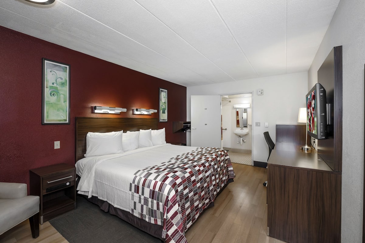 A hotel room with a large bed, a desk, a chair, a TV, and a bathroom visible through an open door.