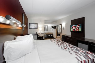 A hotel room with a bed, a desk, a chair, a television, and a mirror.