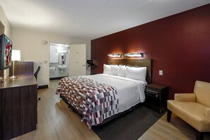 Et hotelværelse med seng, sengebord, stol, skrivebord og et spejl.