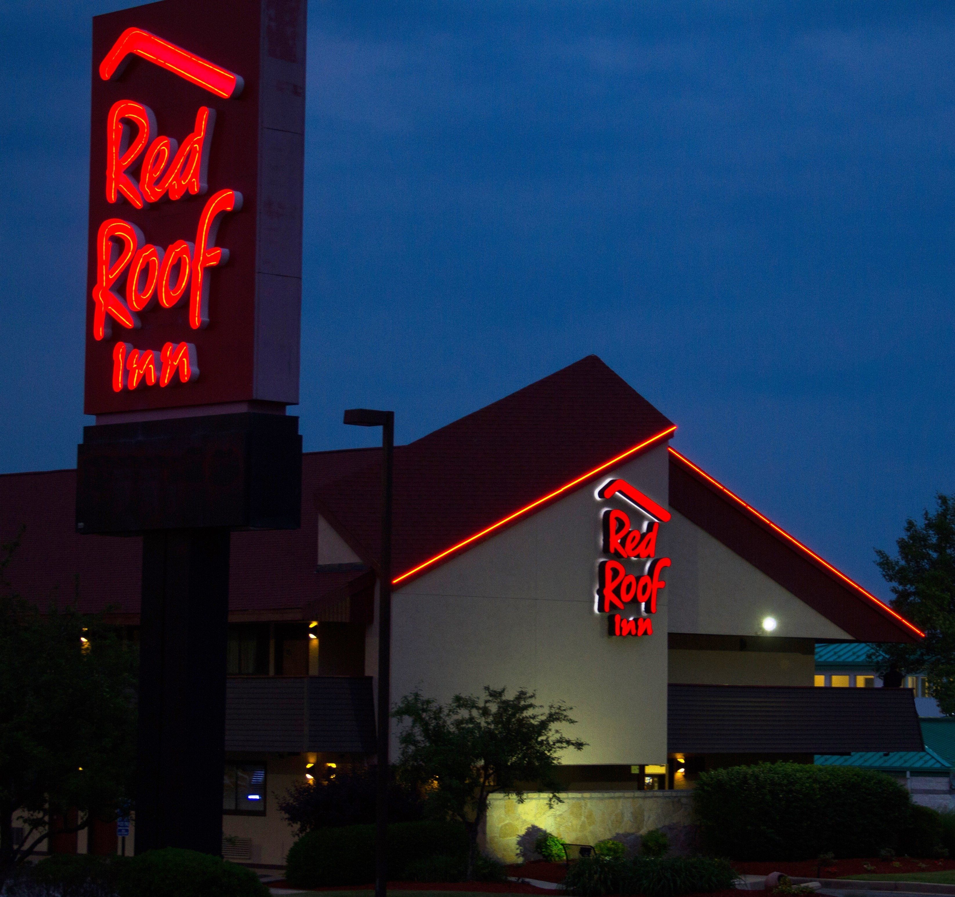 A Red Roof Inn with a prominent neon sign, a red roof, and a modern building facade.