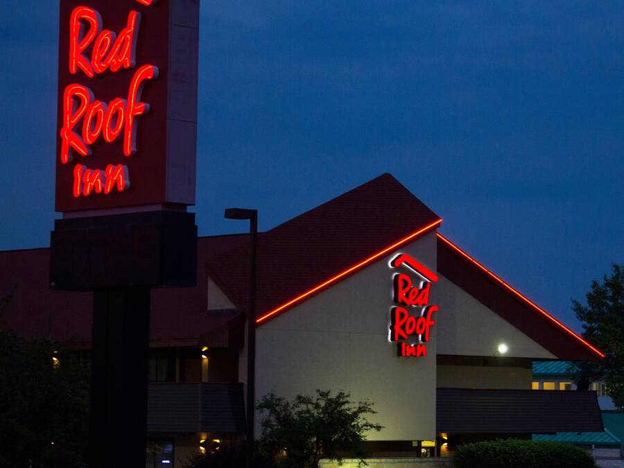 A Red Roof Inn with a prominent neon sign, a red roof, and a modern building facade.