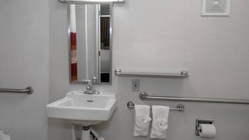 Un baño con lavamanos blanco, espejo, toallero y dispensador de papel higiénico.