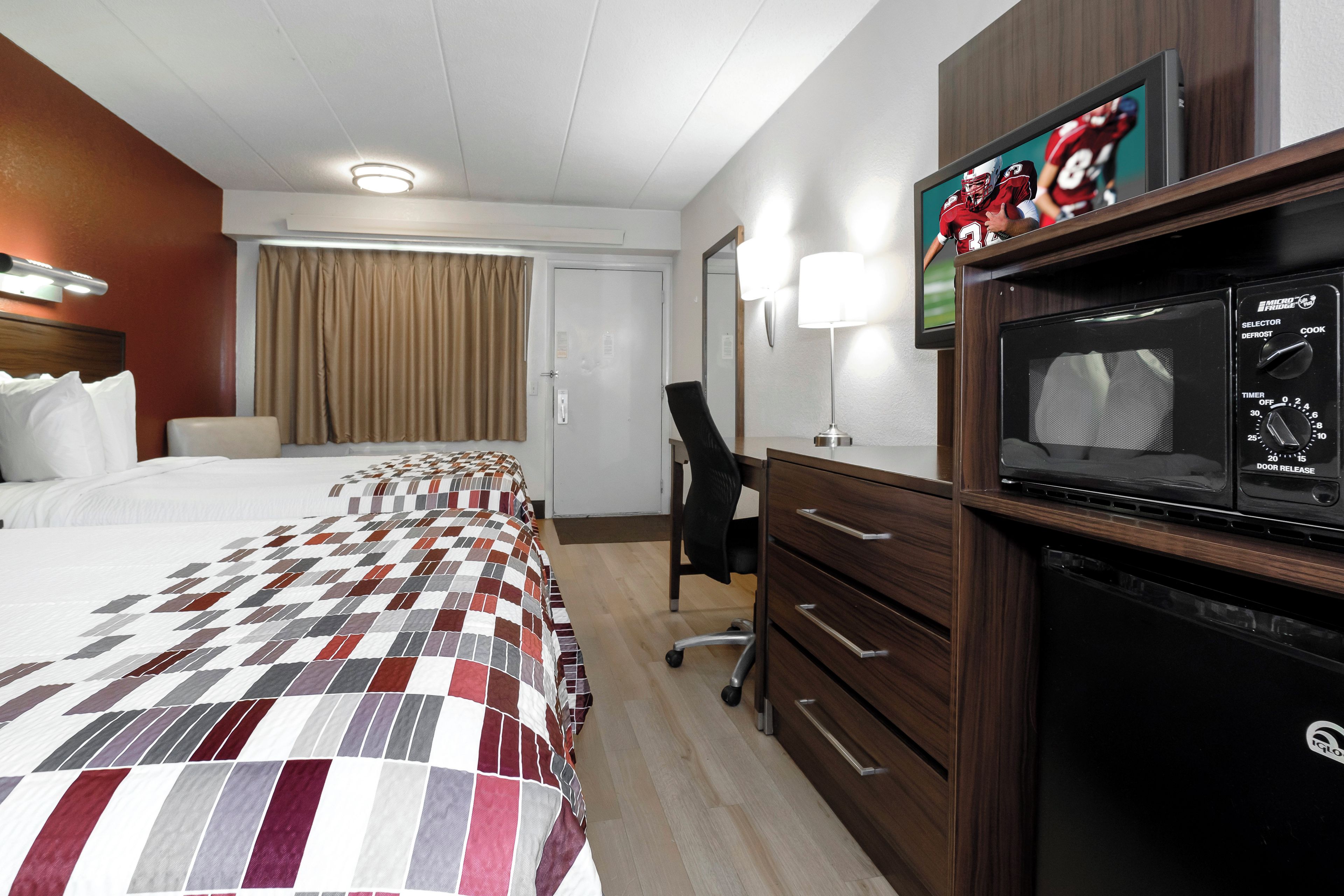 A hotel room with a bed, a desk, a television, and a microwave.