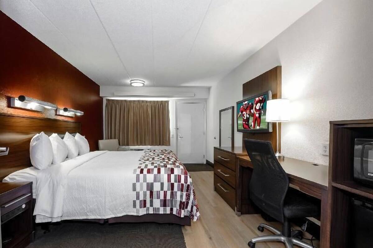 A hotel room with a bed, desk, chair, television, and a door leading to another room.