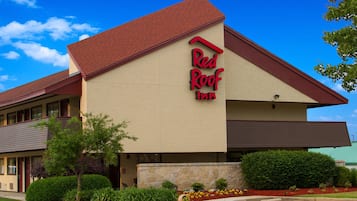 Red Roof Inn features a prominent red roof and a well-manicured landscape with a stone base.