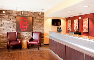 Zona de recepción de Red Roof Inn con pared de piedra, dos sillones de cuero, un taburete de madera, televisor de pantalla plana y obras de arte en la pared.
