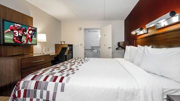A hotel room with a large bed, a television mounted on the wall, a desk with a chair, and a wardrobe.