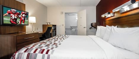 A hotel room with a large bed, a television mounted on the wall, a desk with a chair, and a wardrobe.