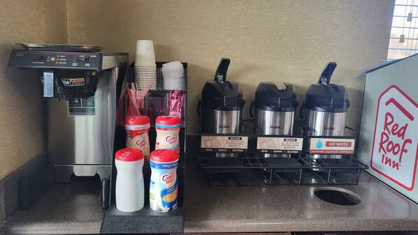 A coffee station with a Bunn coffee maker, paper cups, straws, and various coffee containers including a French vanilla creamer. - Red Roof Inn Aberdeen (Aberdeen)
