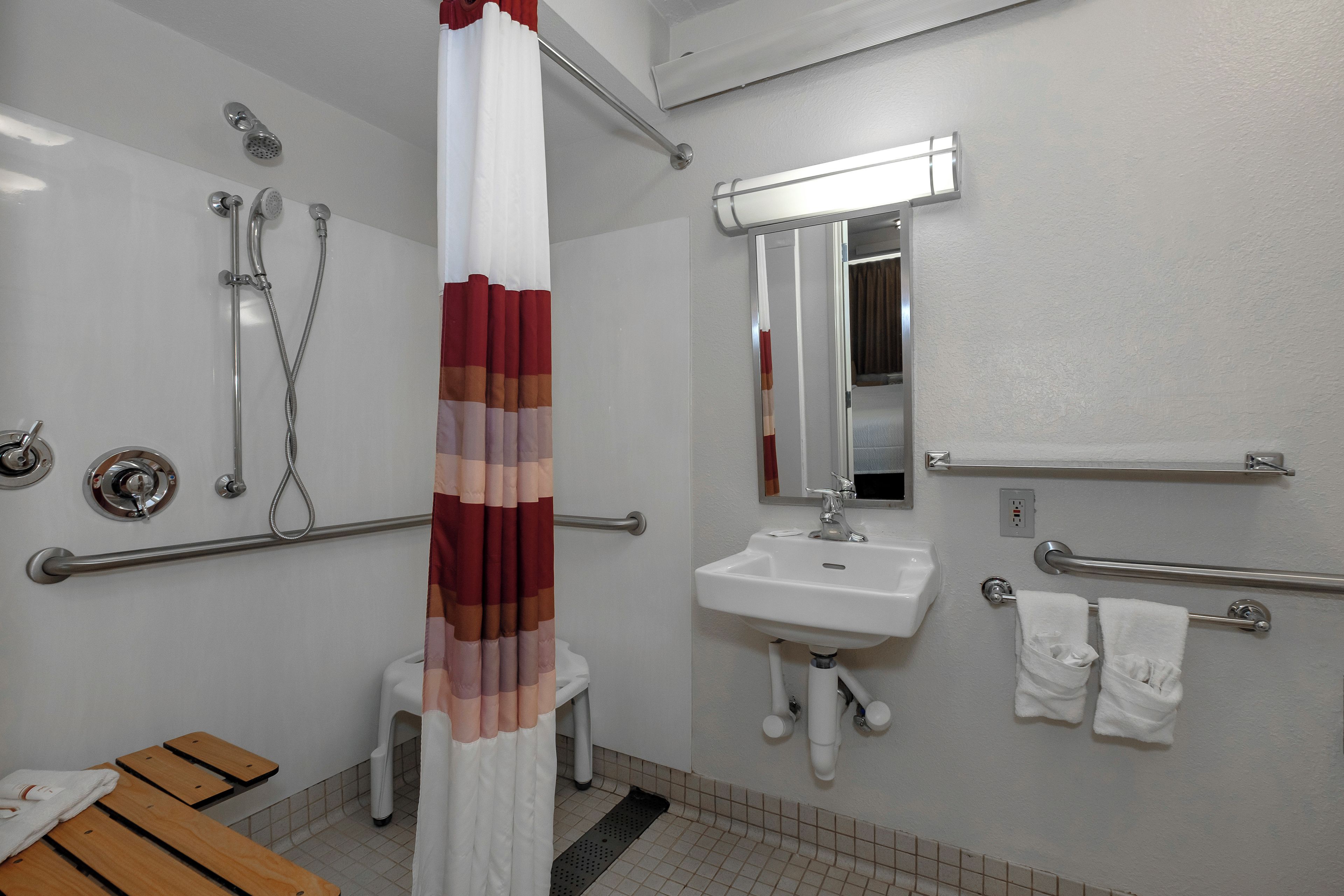 A bathroom with a shower, toilet, sink, and handrails.