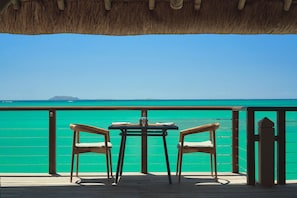A wooden deck with two chairs and a table, overlooking turquoise waters and a distant island. - Paradise Cove Boutique Hotel - Adults only (Cap Malheureux)