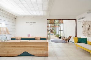 A reception area with a wooden desk, a sofa, and a chair. The wall has a sign that reads "CINQ MÔNDES PARIS".
