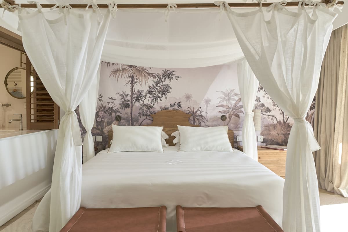 A bed with a canopy, a headboard with a floral mural, and a wooden nightstand.