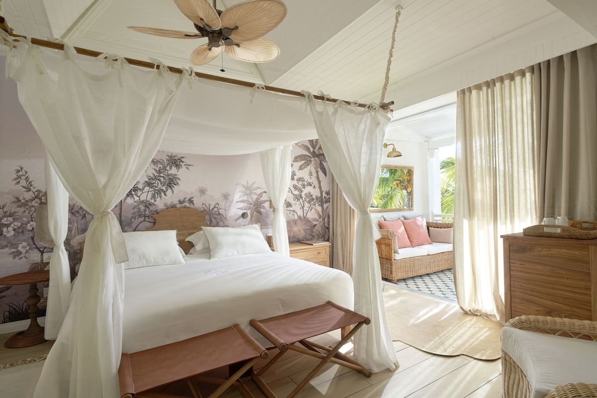 A bedroom with a bed, canopy, wooden furniture, and a view of the outdoors.