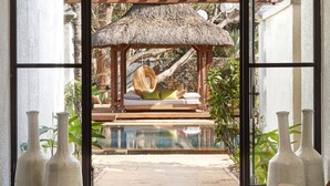 A room with a large window, a wooden chair, and a thatched-roof structure with a pool. - Paradise Cove Boutique Hotel - Adults only (Cap Malheureux)