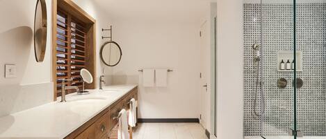 A modern bathroom with a wooden vanity, a large mirror, a glass shower enclosure, and a tiled floor.