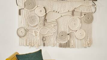 A yellow sofa with a green cushion and a macrame wall hanging above it.