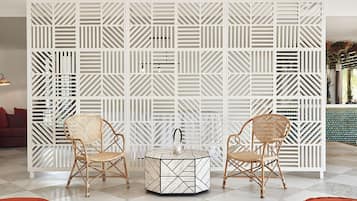 A room with a white geometric-patterned partition, two wicker chairs, a round table with a geometric design, and a red sofa.