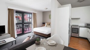A modern hotel room with a bed, a dining area, a kitchen, and a balcony with chairs. - BreakFree Adelaide (Adelaide)
