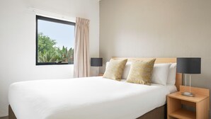 A neatly made bed with white linens, two bedside tables with lamps, and a window with curtains. - BreakFree Adelaide (Adelaide)