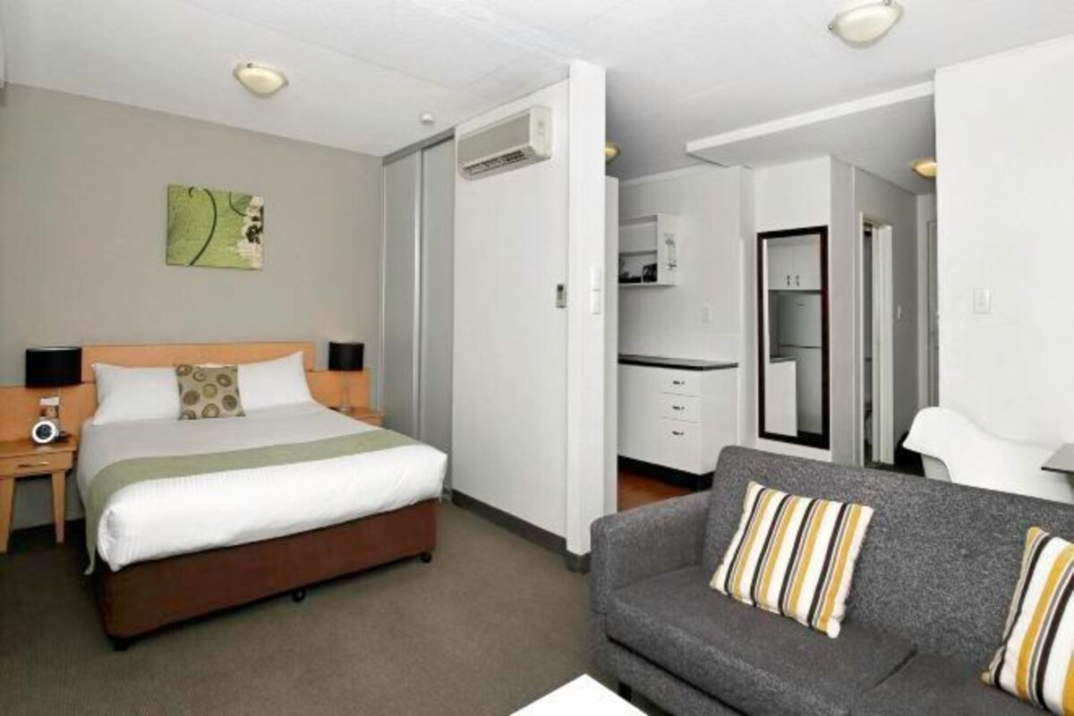 A hotel room with a bed, a sofa, a desk, and a kitchenette.