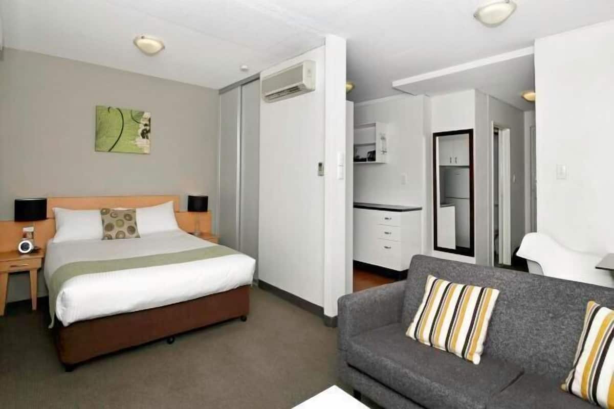 A hotel room with a bed, a sofa, a desk, and a kitchenette.