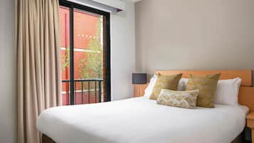 Ein Hotelzimmer mit einem großen Bett, einem Fenster mit Vorhängen, einem hölzernen Kopfteil und einem Nachttisch mit Lampe.
