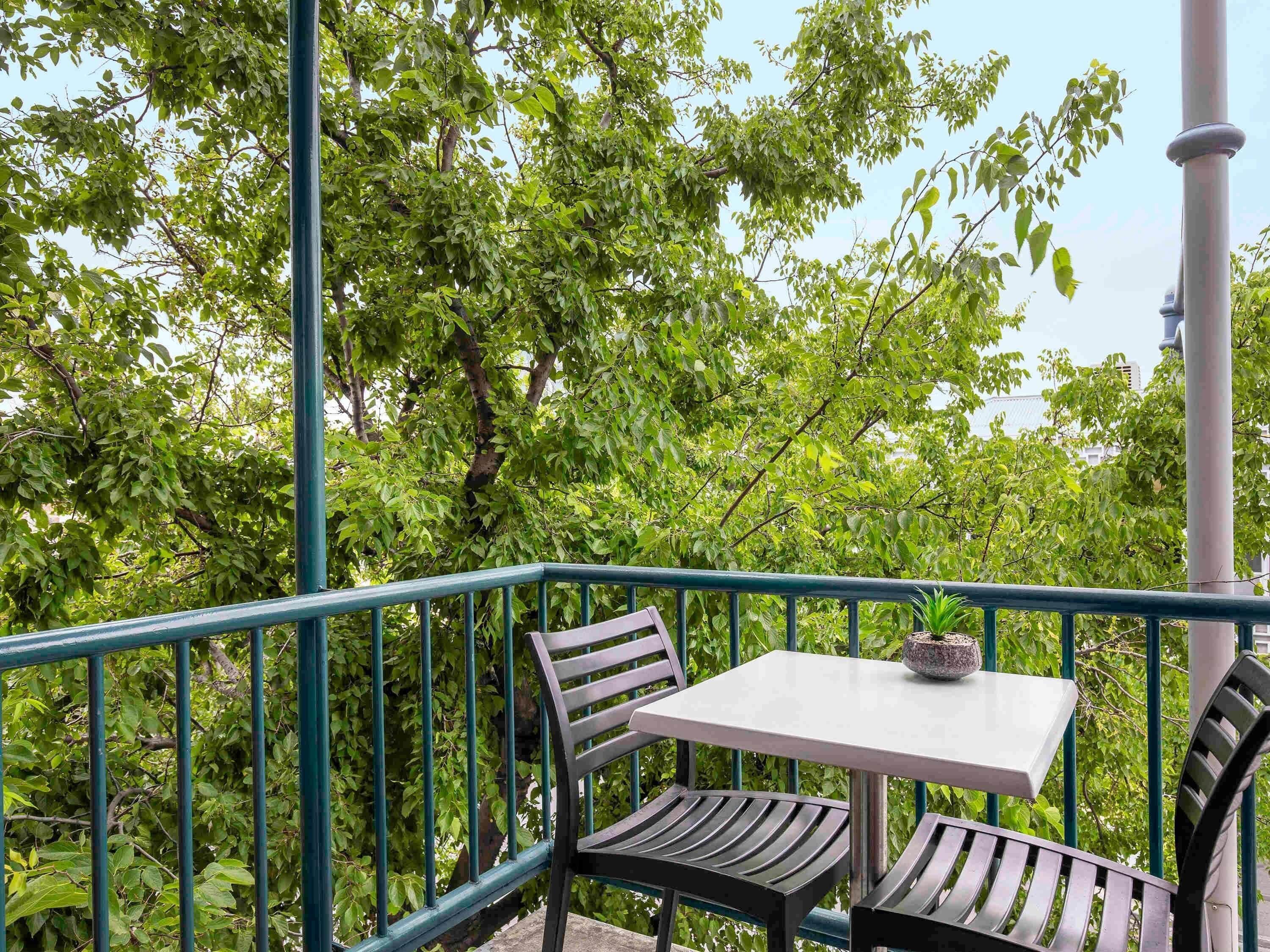 A balcony with a table and chairs, surrounded by greenery.