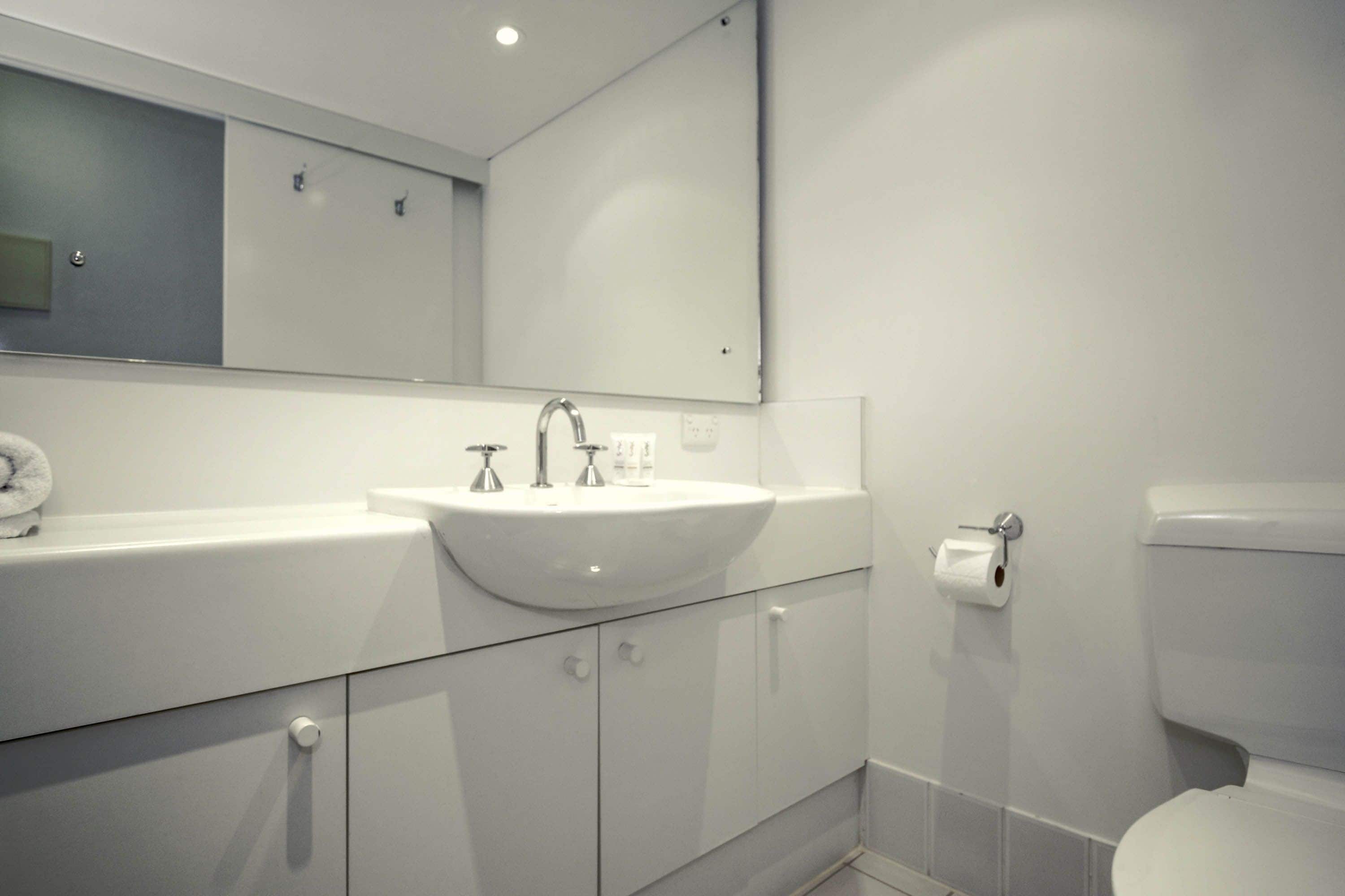 A modern bathroom with a white sink, mirror, and toilet.