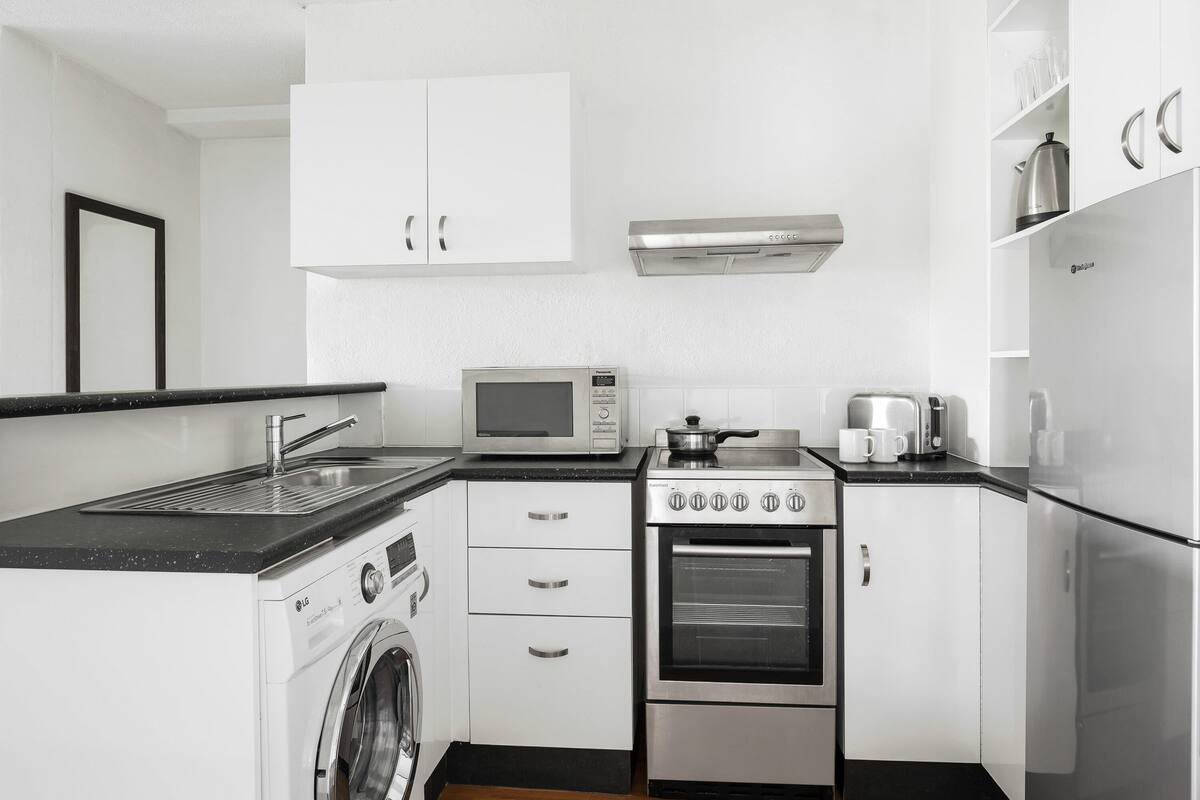A compact kitchen with a washing machine, microwave, stove, and a refrigerator.