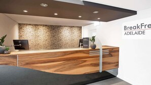 A reception area with a wooden reception desk, a computer, a plant, and a wall with a tree pattern. - BreakFree Adelaide (Adelaide)