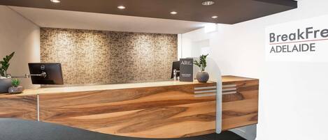 A reception area with a wooden reception desk, a computer, a plant, and a wall with a tree pattern.