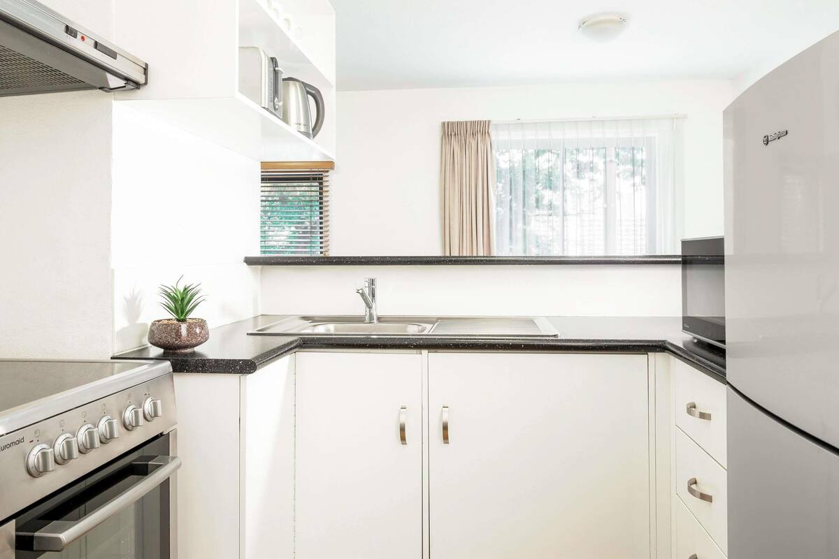 A kitchen with white cabinets, a stainless steel stove, a sink, and a window with curtains.