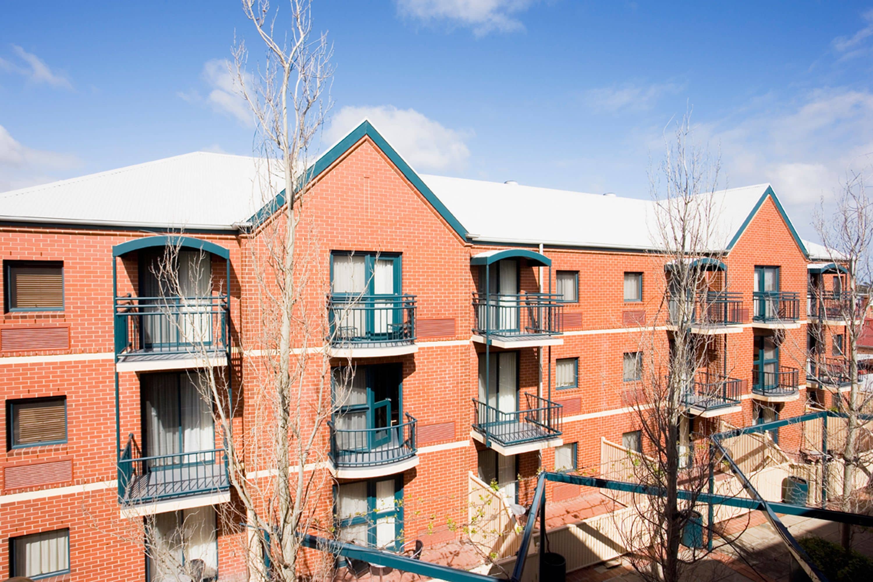 A multi-story brick building with balconies, a flat roof, and a clear sky.
