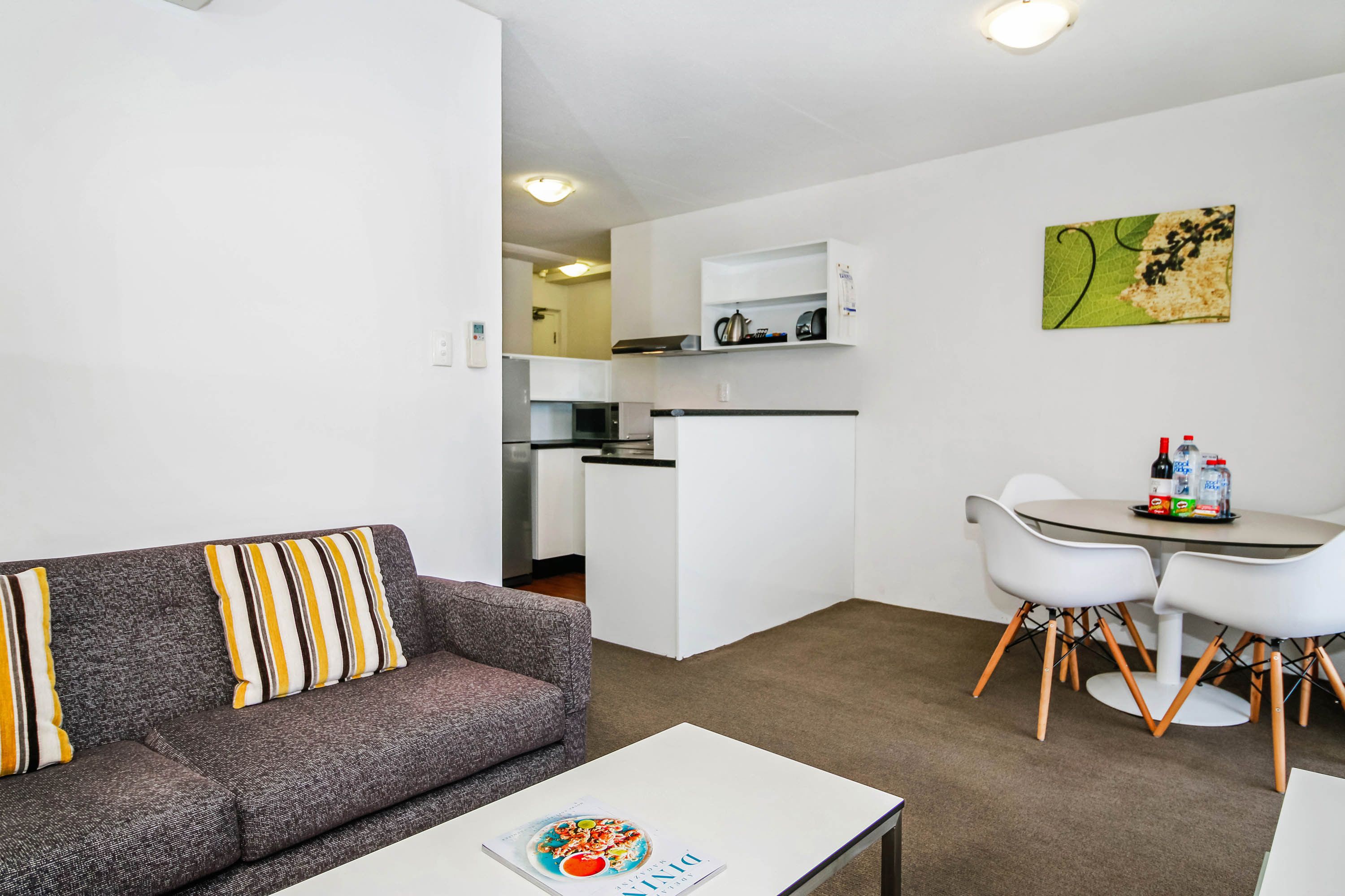 Ein modernes Wohnzimmer mit einem grauen Sofa, einem Couchtisch und einem Essbereich mit weißen Stühlen und einem kleinen Tisch.