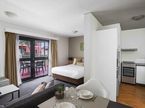 Quarto de hotel com cama, mesa para dois, cozinha compacta e varanda com vista para edifícios.