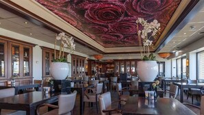 A spacious restaurant with high ceilings and a unique ceiling design. Tables are arranged in a casual layout with comfortable seating.