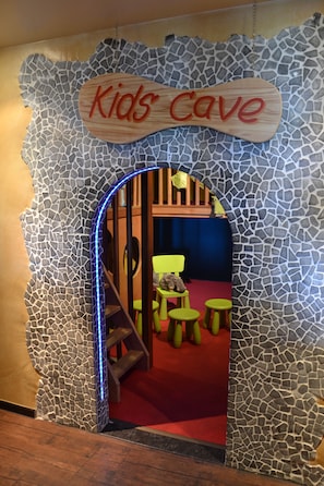 A children's play area with a 'Kids Cave' sign, a wooden bench, and green stools. - Fletcher Hotel-Restaurant Heiloo (Heiloo)
