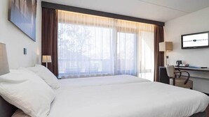 A hotel room with a large bed, a desk with a computer, and a TV on the wall.