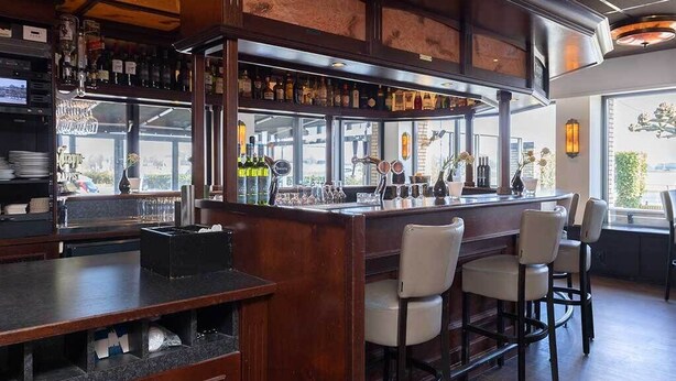 A bar area with a wooden counter, bar stools, and a variety of bottles and glasses.