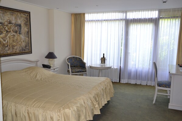A hotel room with a large bed, a chair, a small table with a bottle, and a painting on the wall. - Fletcher Hotel-Restaurant Heiloo (Heiloo)