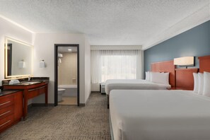 Habitación de hotel con baño, cama, escritorio y silla, y un espejo grande.