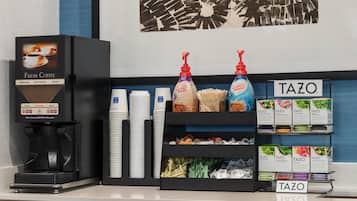 Una estación de café con una máquina de café, vasos desechables y diferentes tipos de cápsulas.
