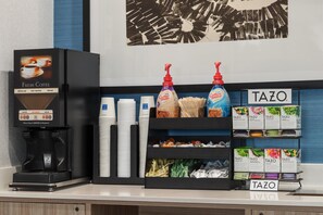 Una estación de café con una máquina de café, vasos desechables y diferentes tipos de cápsulas.