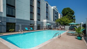 A swimming pool with lounge chairs and umbrellas, surrounded by a building with multiple windows and a tree. - Hyatt Select Nashville/Opryland (Nashville)