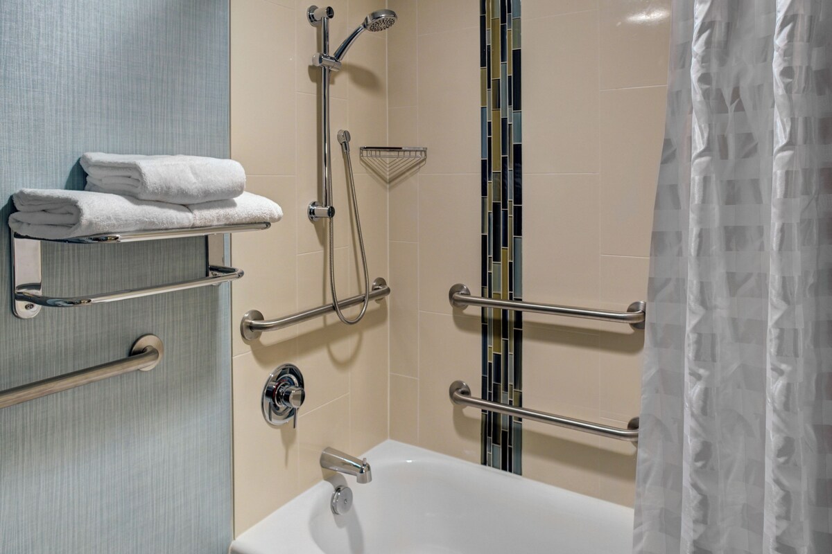 Un baño con bañera, barras de apoyo, toallero y cabezal de ducha.